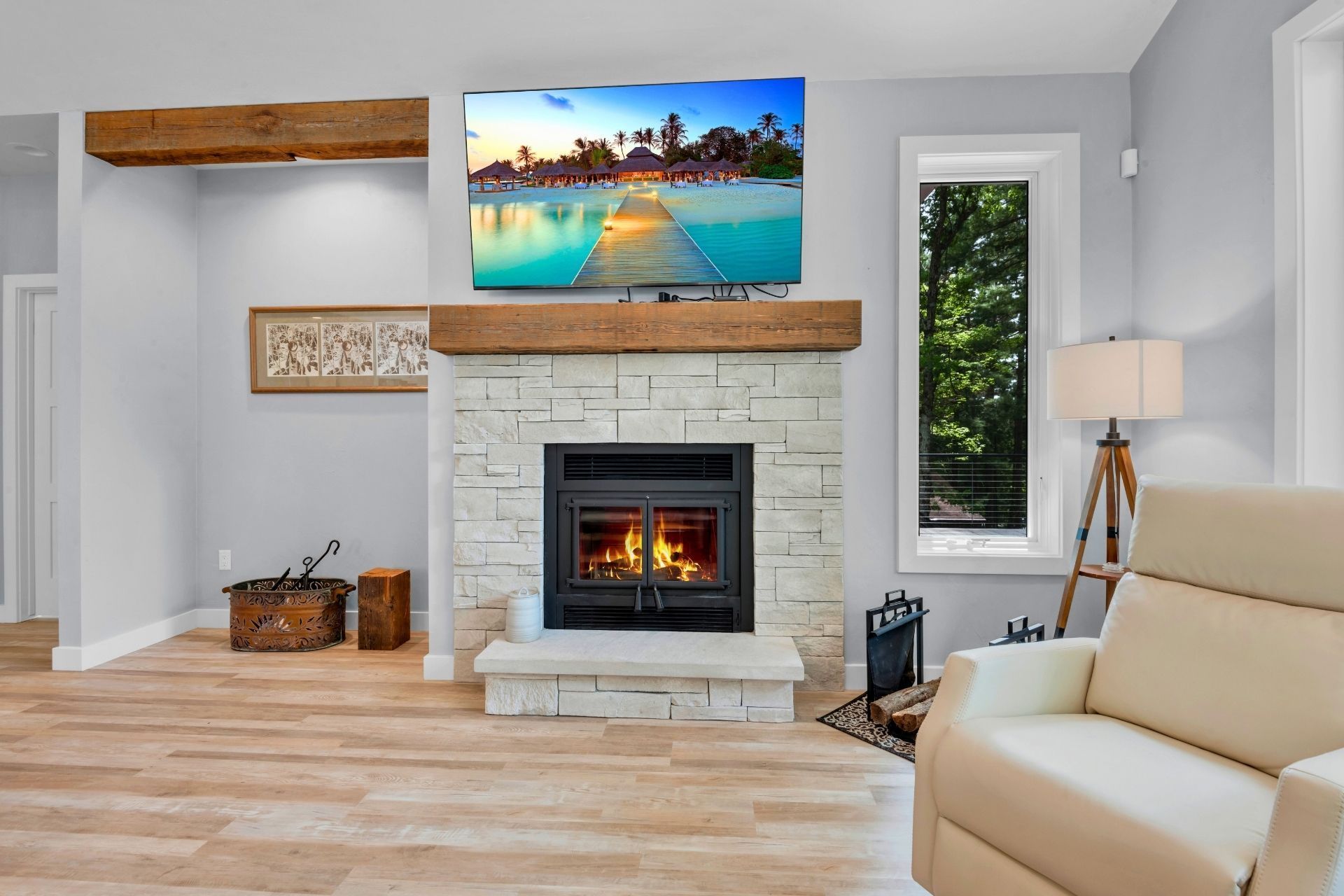 Living room with a fireplace, TV, and white recliner. Light wood floors and gray walls.