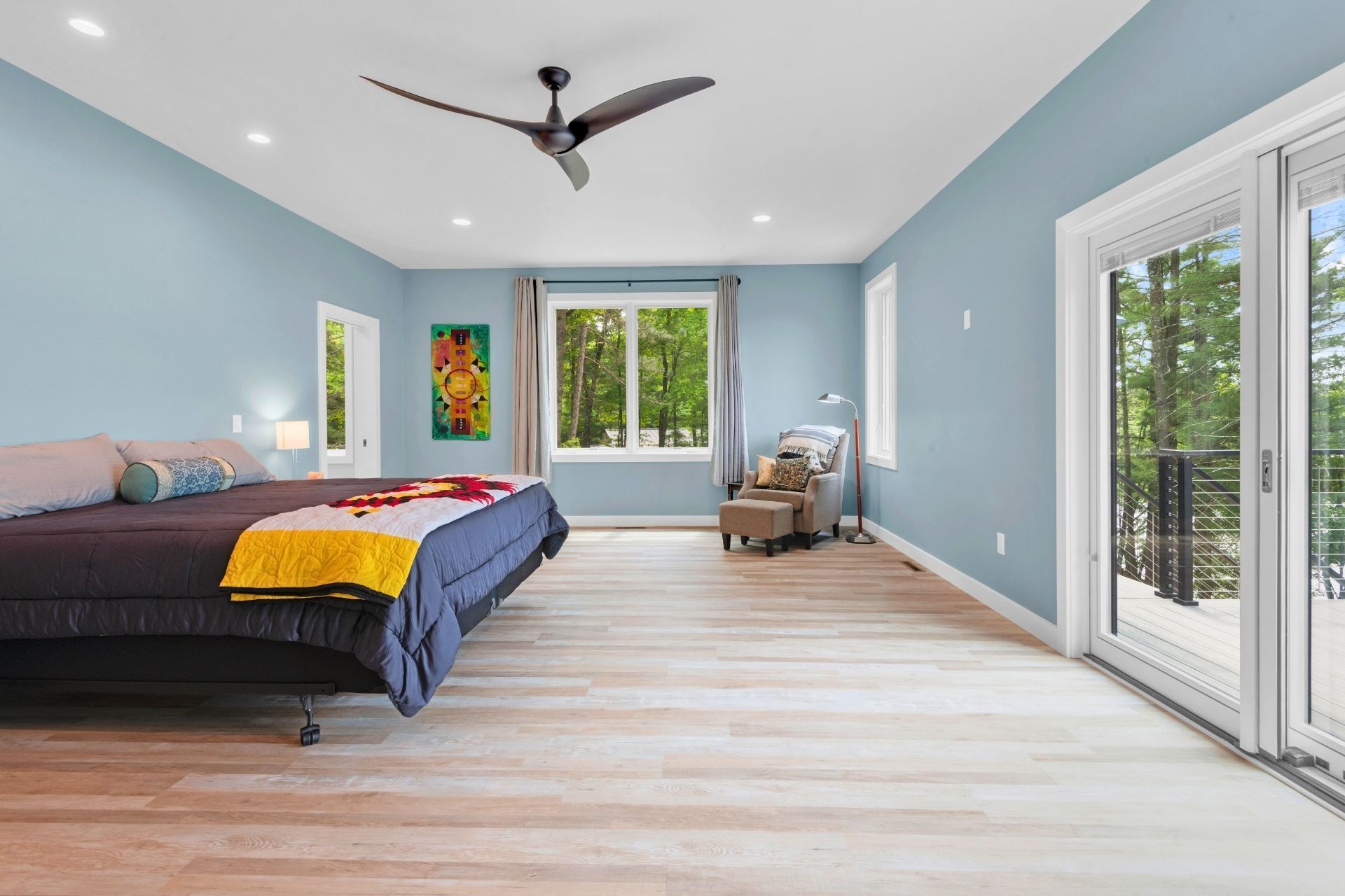 A large bedroom with a bed , chair , sliding glass doors and a ceiling fan.
