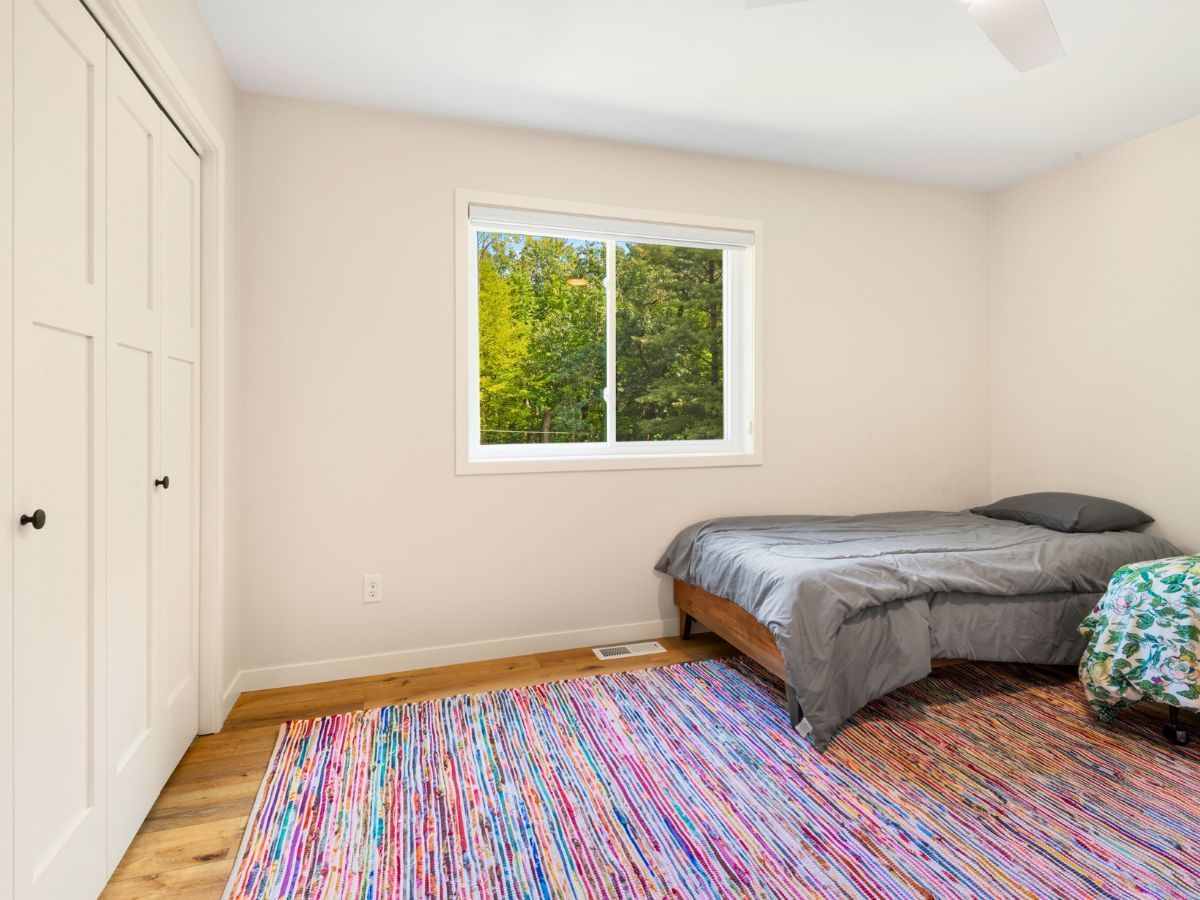 A bedroom with a bed , rug , window and closet.