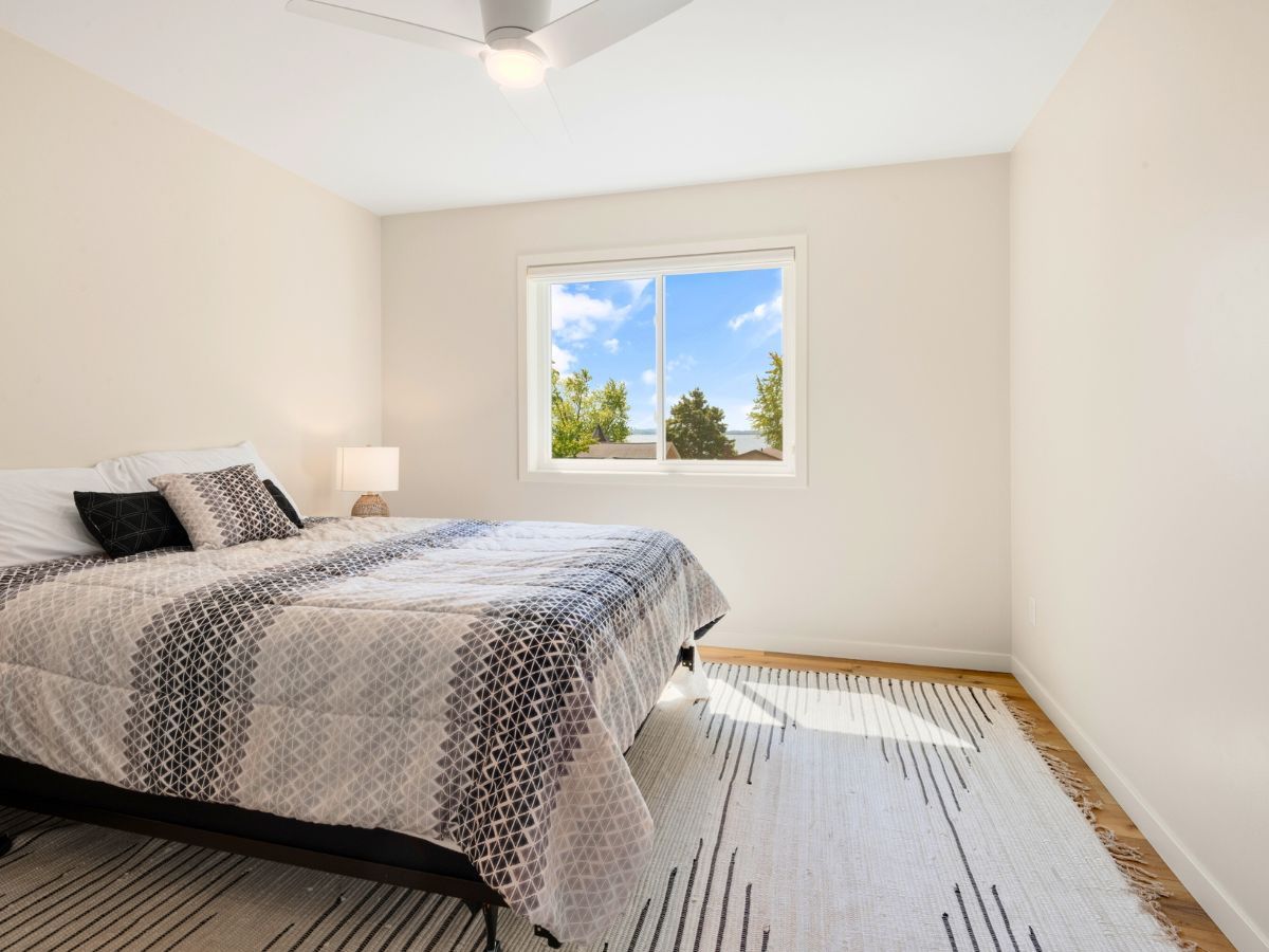 A bedroom with a bed , rug , window and ceiling fan.