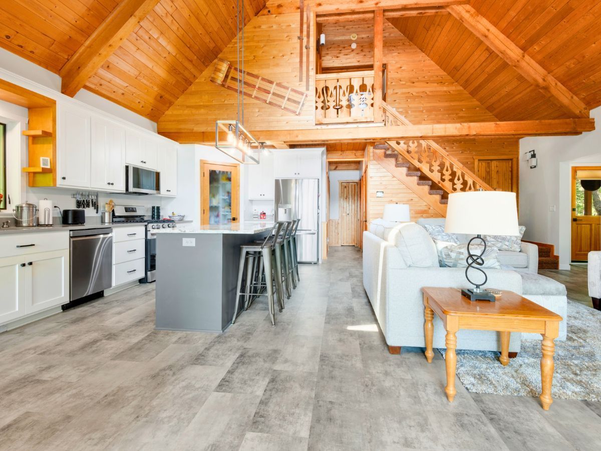 A living room and kitchen in a log cabin with a wooden ceiling.