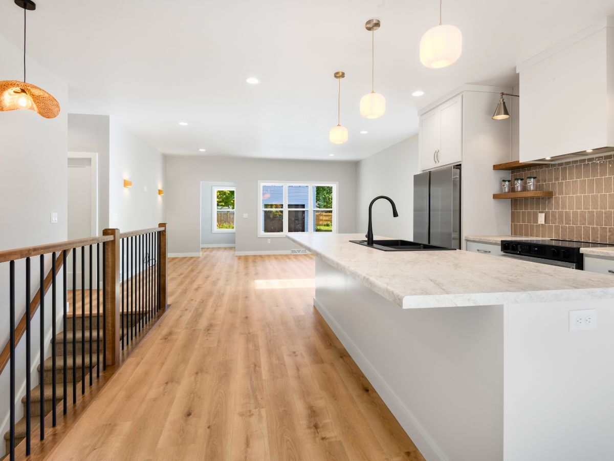 A kitchen with hardwood floors , white cabinets , a sink , and a refrigerator.