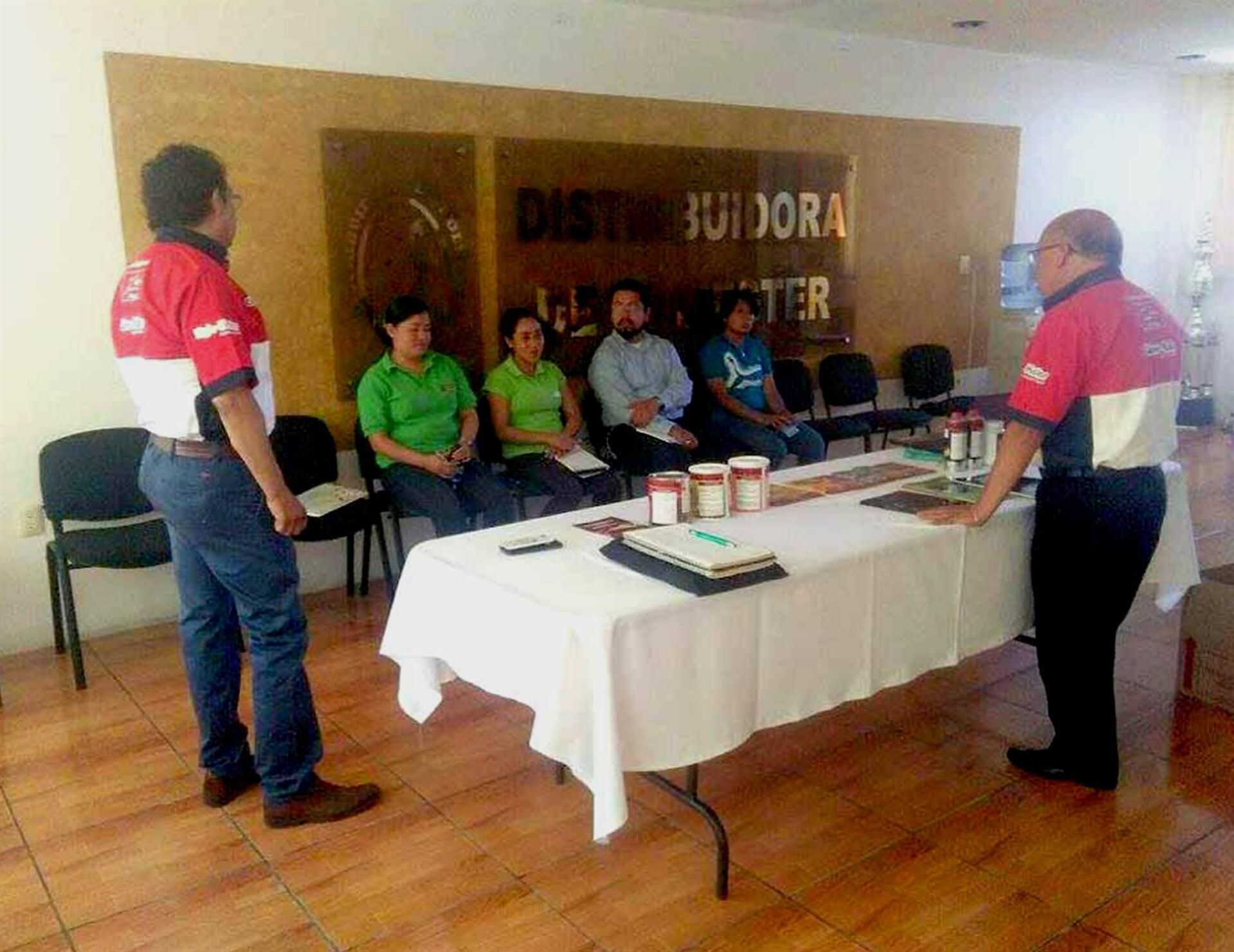 Un grupo de personas se sienta alrededor de una mesa frente a una pared que dice distribuidora