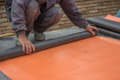 Un hombre está arrodillado y enrollando un rollo de alfombra.