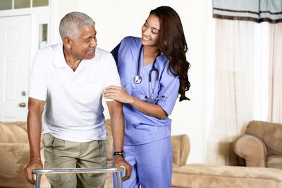 Caregiver assisting a patient with a walker in a living room, both smiling
