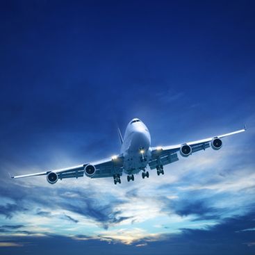 Commercial airplane descending against a blue sky with landing gear down and bright clouds below