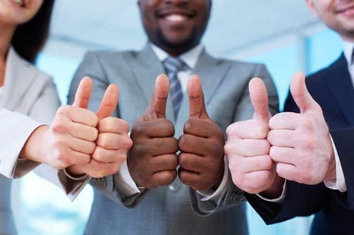 Team of business people in suits giving thumbs up in an office setting