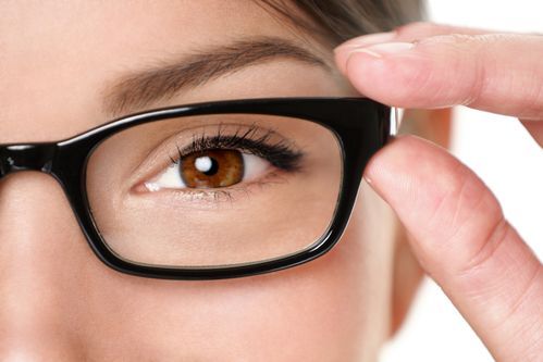 Close-up of a person adjusting black eyeglasses over one eye