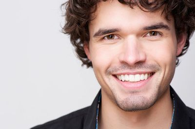 Smiling man with curly hair in a dark jacket on a light background