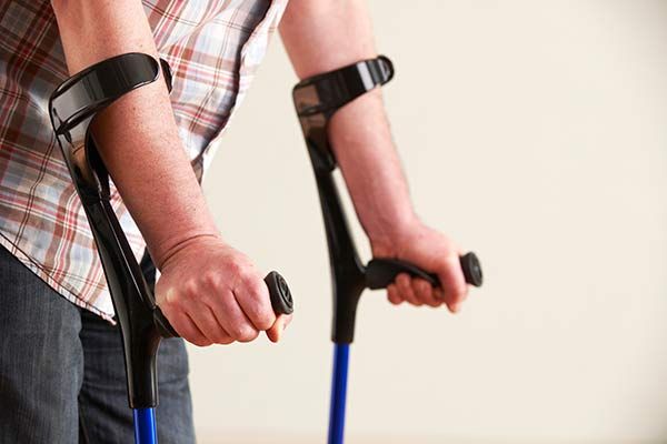 Person using forearm crutches with black hand grips and blue shafts indoors
