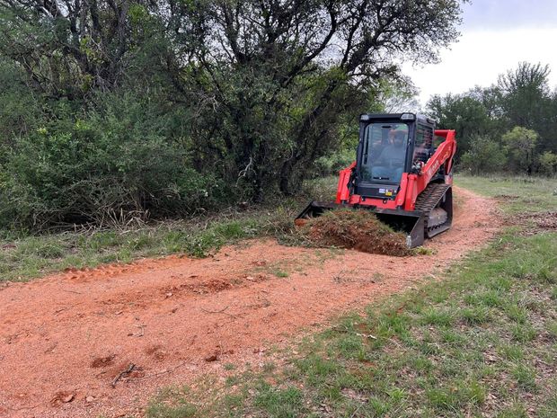 Red skid steer building a trail through grass, pushing dirt.