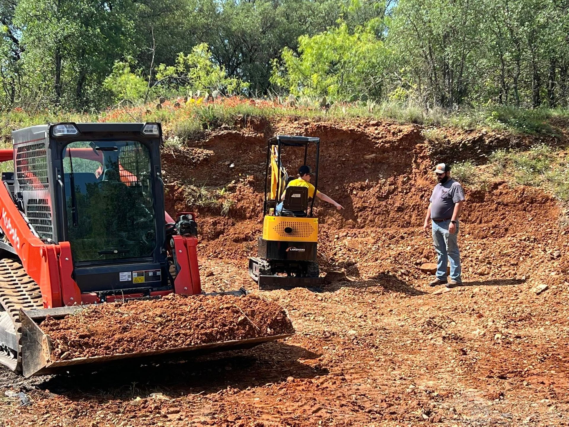 A man standing near a small excavator and a skid steer on a construction site.