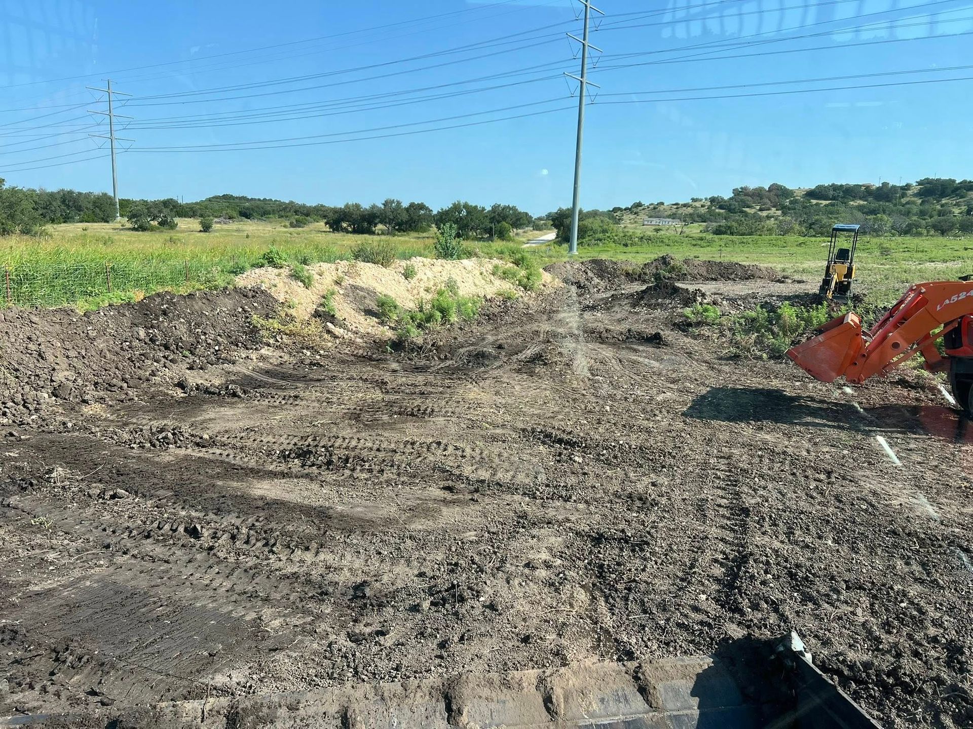 Construction site with dirt, a small excavator, and a pile of sand under a blue sky.
