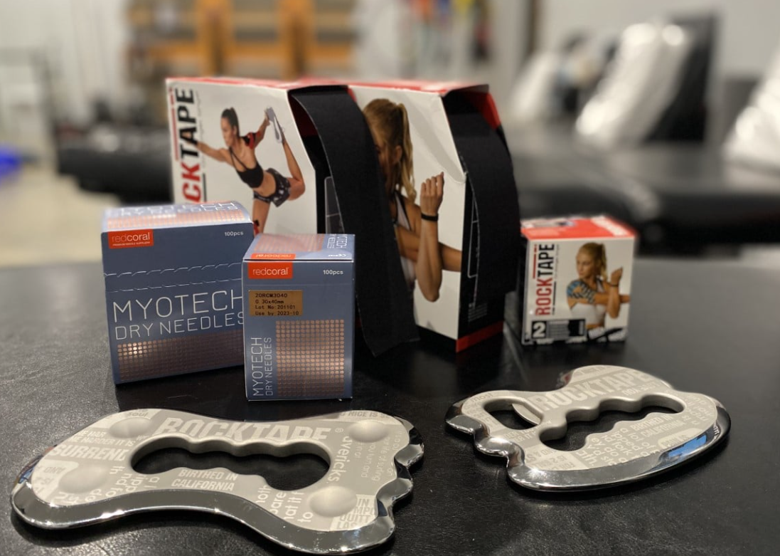 A table topped with boxes of kinesio tape and a foot massager.
