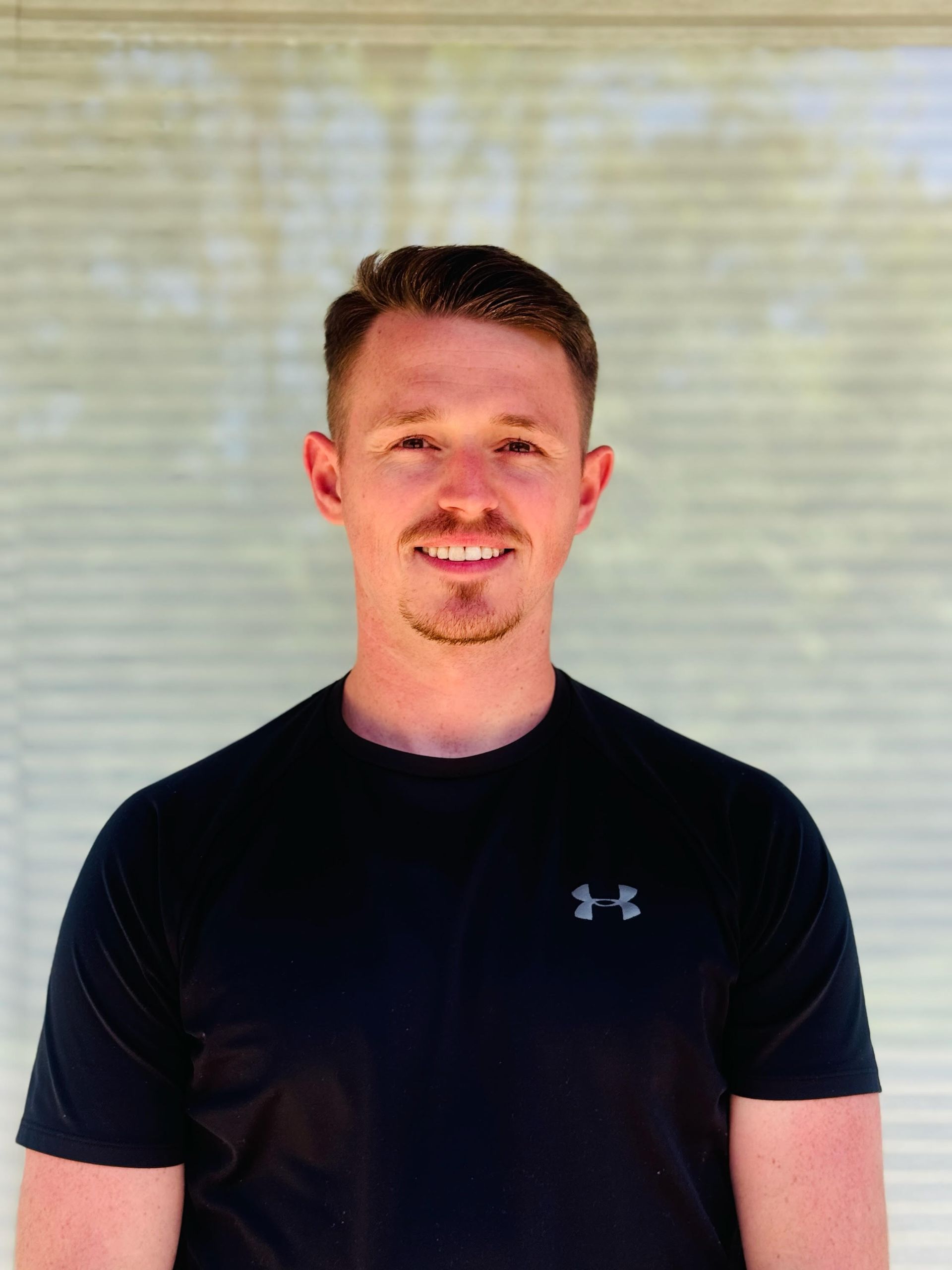 A man wearing a black under armour shirt is smiling for the camera.