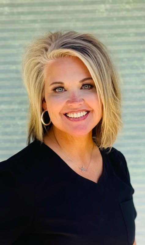 A woman wearing a black shirt and earrings is smiling for the camera.