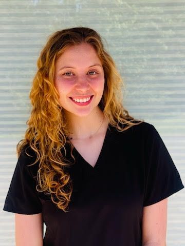A woman in a black scrub top is smiling for the camera.