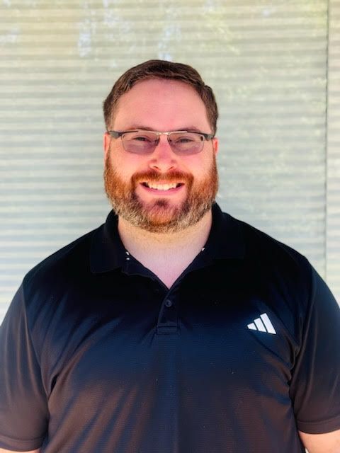 A man with a beard and glasses is wearing a black adidas shirt.