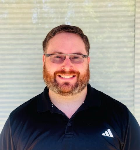 A man with a beard and glasses is wearing a black adidas shirt