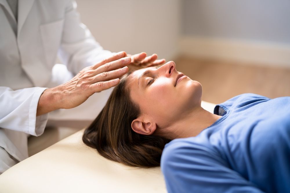 A woman is laying on a table getting a healing treatment from a doctor.