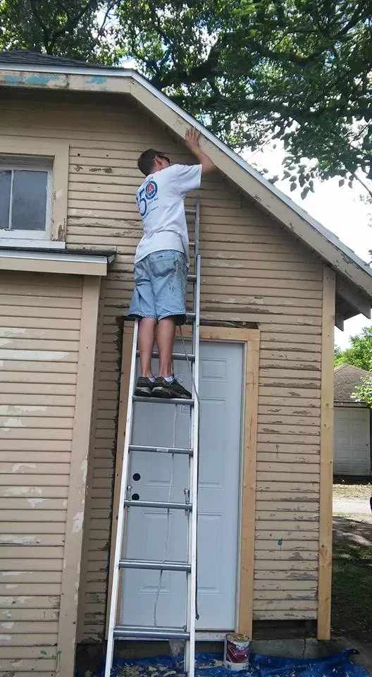 A man is standing on a ladder on the side of a house.