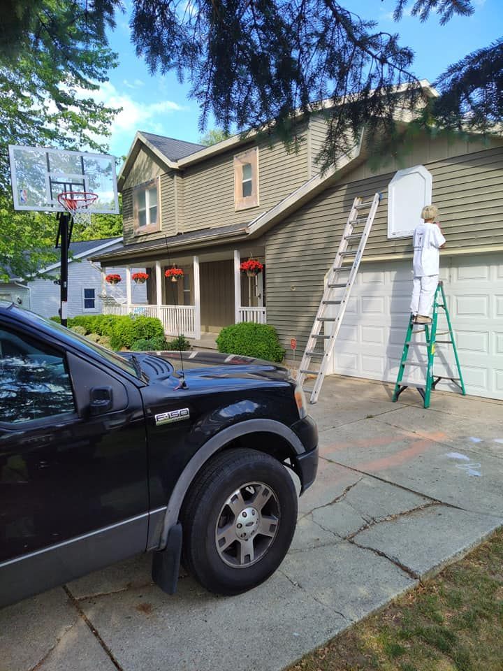A man on a ladder is painting the side of a house.