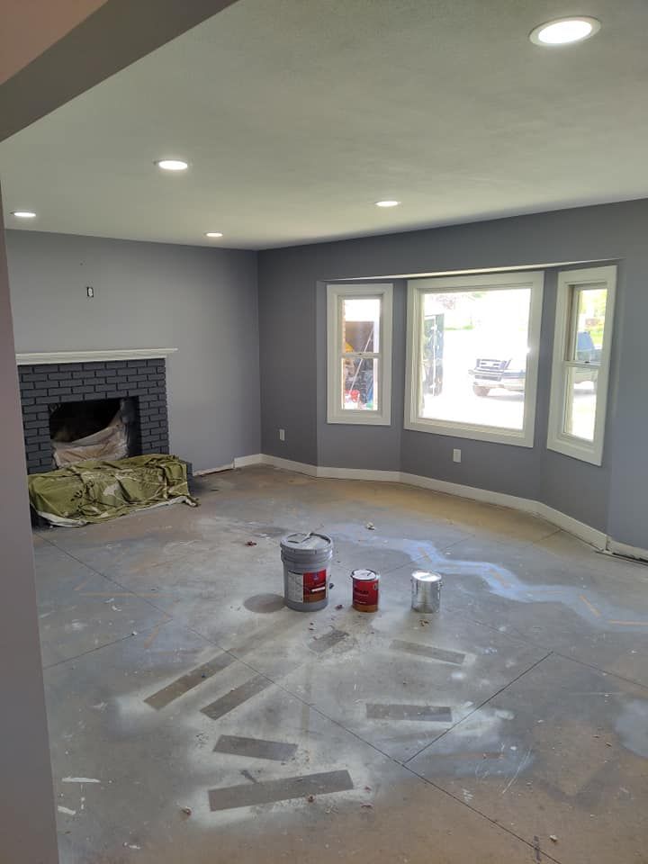 A living room with a fireplace and buckets of paint on the floor.