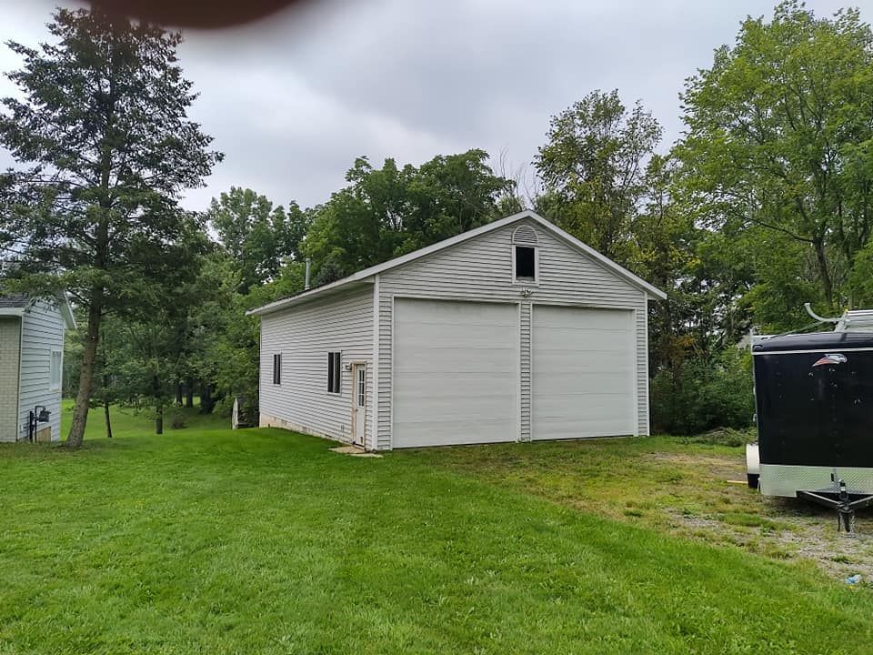 A white garage with a black trailer parked in front of it