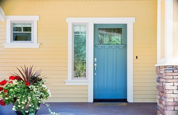 A yellow house with a blue door and a potted plant in front of it.