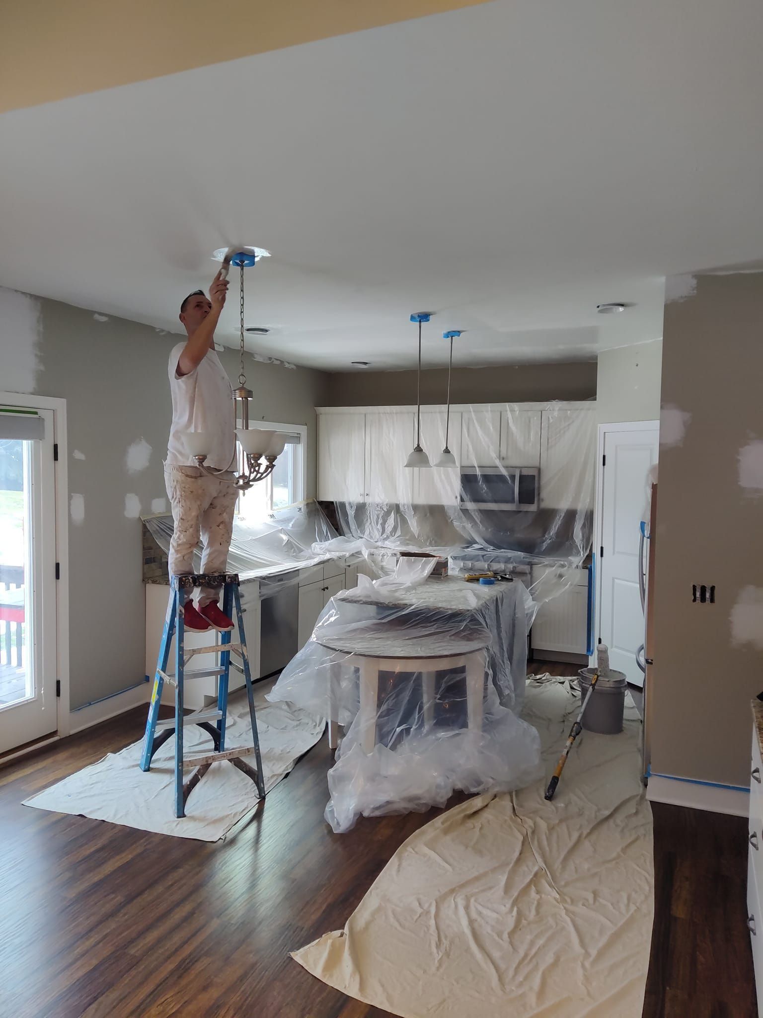 A man is standing on a ladder in a kitchen painting the ceiling.