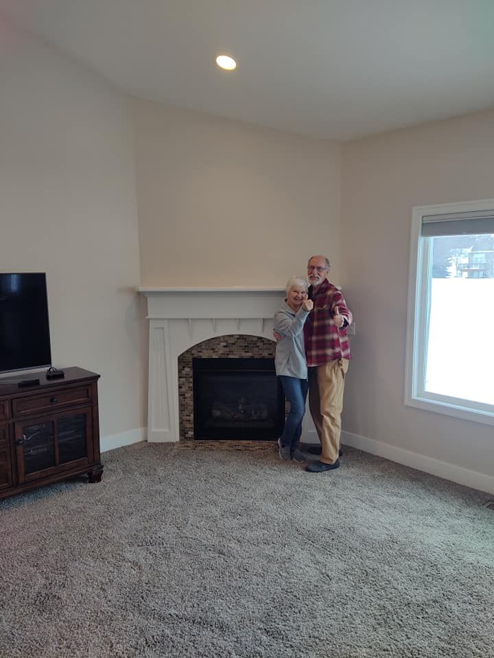 A man and a woman are standing in front of a fireplace in a living room.
