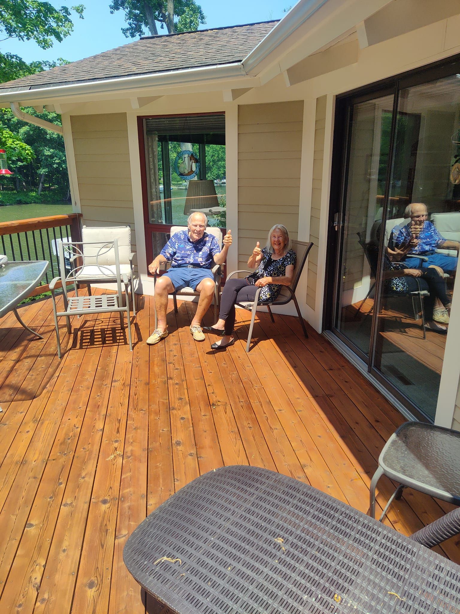 Two people are sitting on a wooden deck in front of a house.