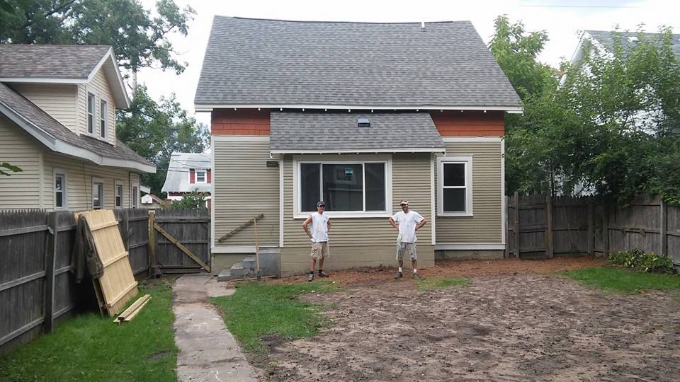 Two men are standing in front of a small house