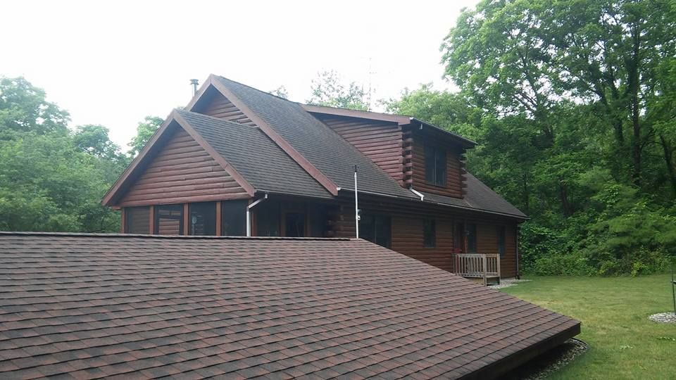 A large log cabin with a black roof is surrounded by trees.