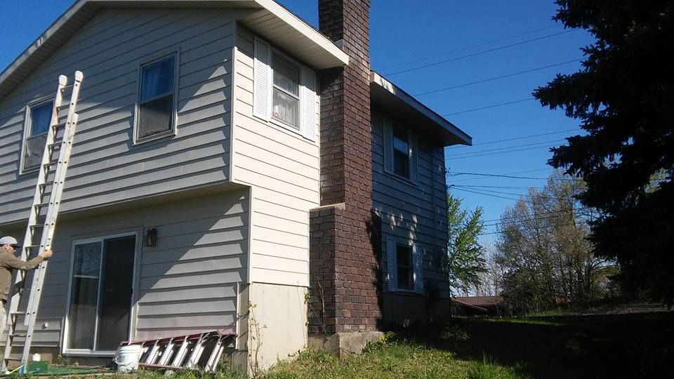 A man on a ladder is painting the side of a house