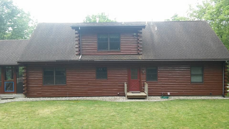 A large log cabin with a gray roof and a red door.