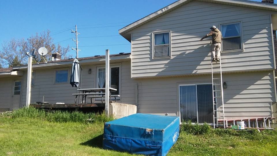 A man on a ladder is painting the side of a house.