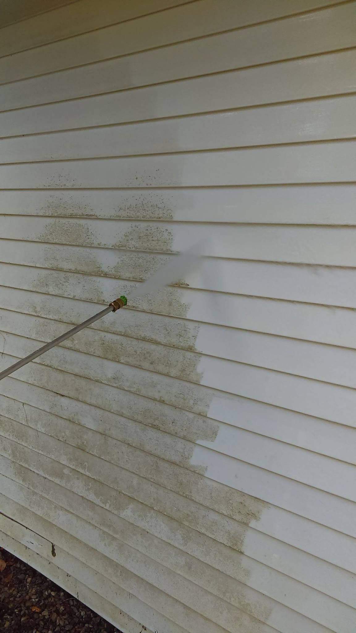 A person is cleaning the side of a house with a pressure washer.