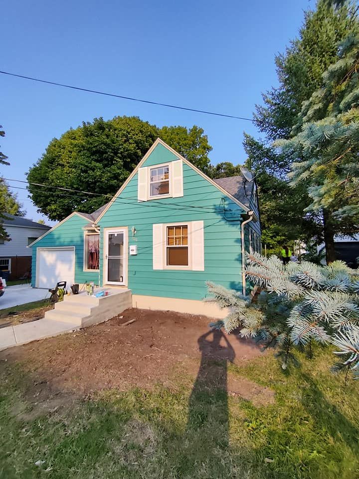 A small green house with white shutters and a garage.