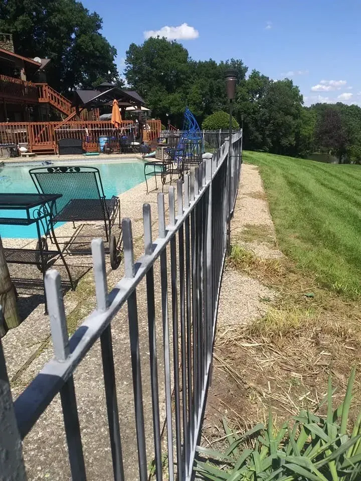 A metal fence surrounds a swimming pool with chairs and tables.