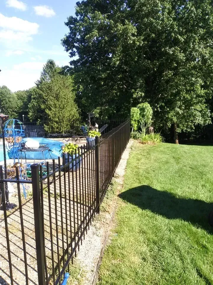 A wrought iron fence surrounds a swimming pool in a backyard.