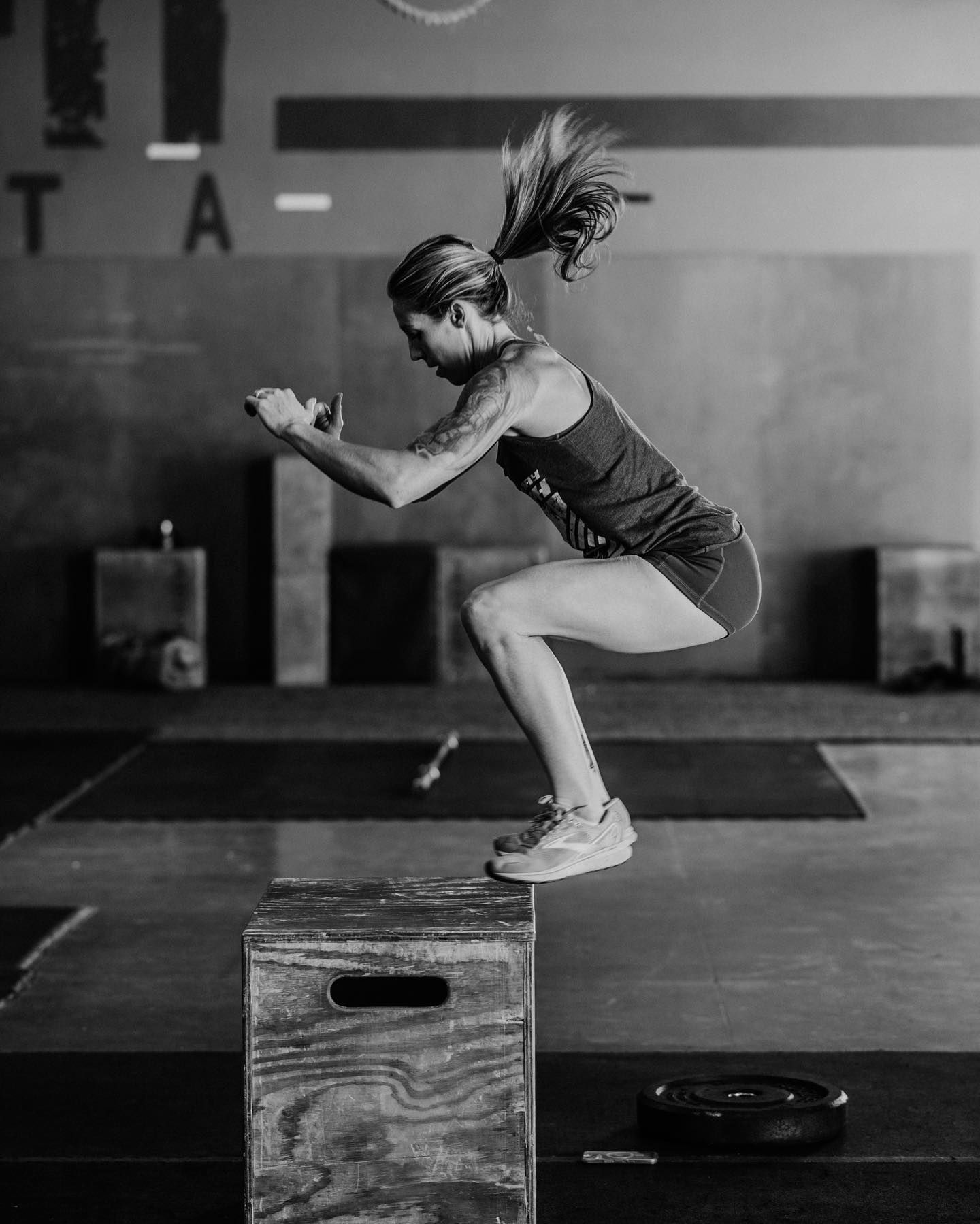 A woman is jumping on a wooden box in a gym.