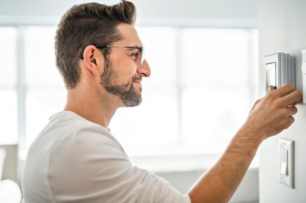 a man is adjusting a thermostat on a wall .