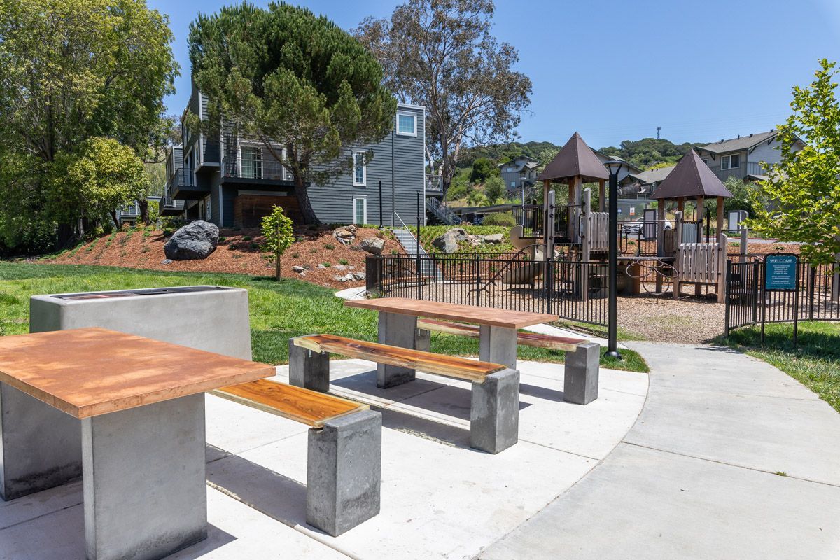 Outdoor community area with a playground, picnic tables, and a curved concrete walkway.