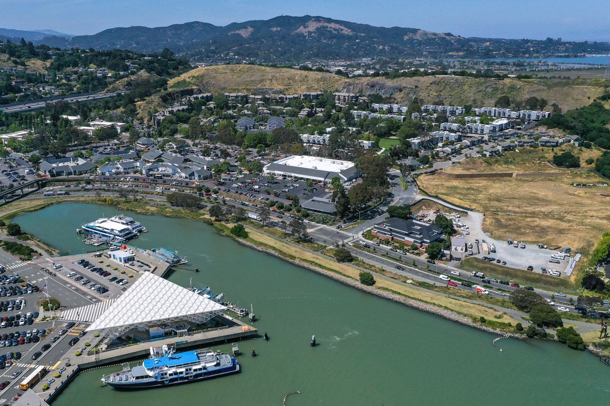 Aerial view of a waterfront apartment community with marina, parking, and surrounding hills.