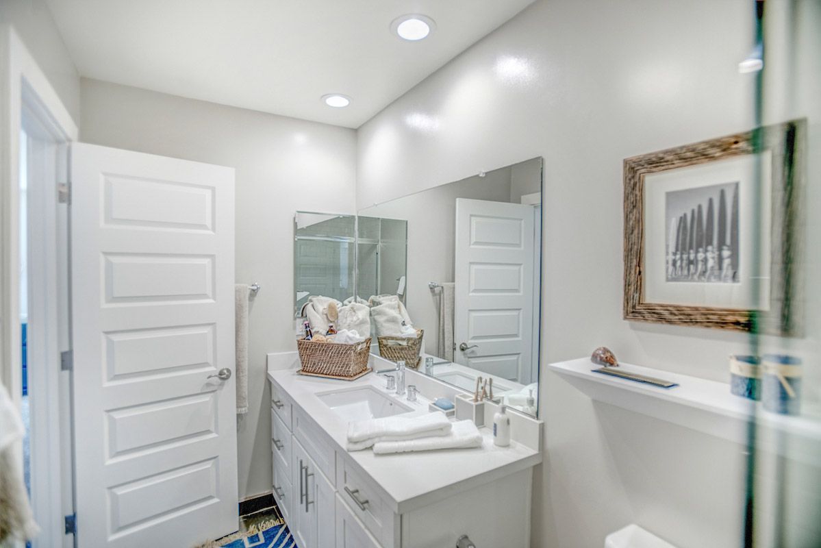 Bright bathroom with a white double vanity, large mirror, and baskets of towels.