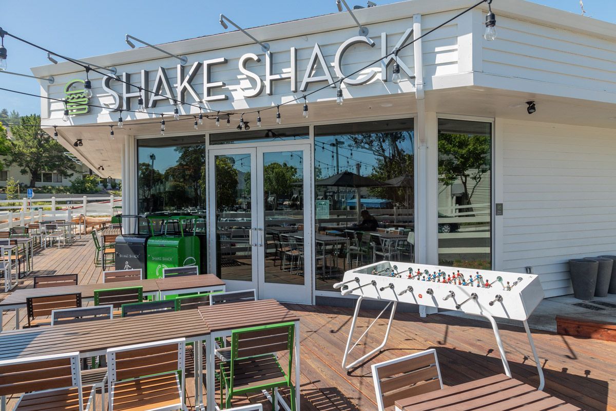 Exterior view of a Shake Shack at an apartment community with outdoor seating and string lights.