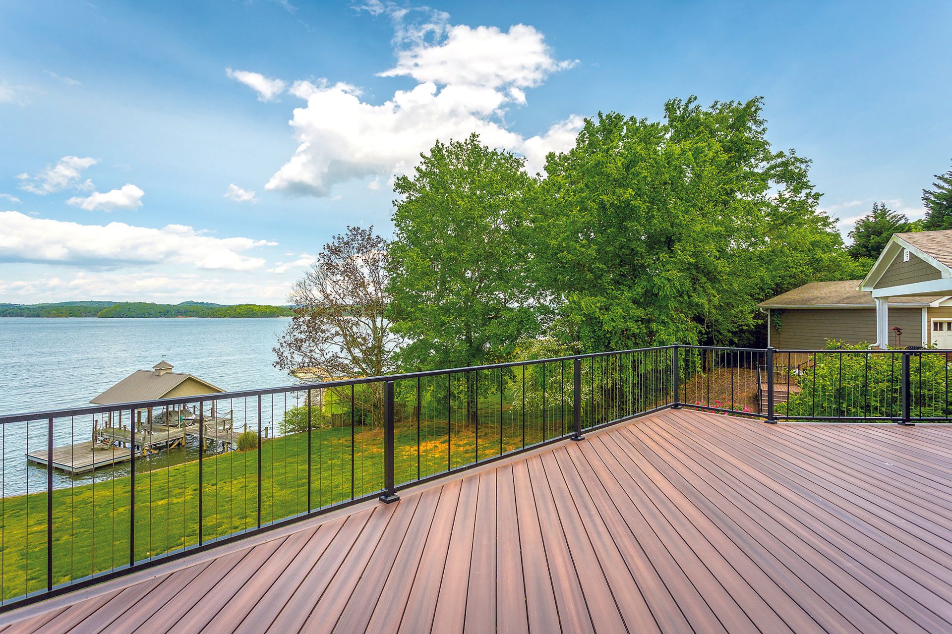 A large wooden deck with a railing overlooking a lake.