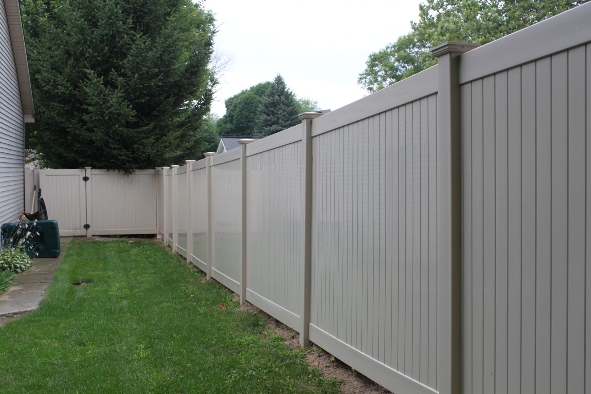 A white fence surrounds a lush green yard in front of a house.