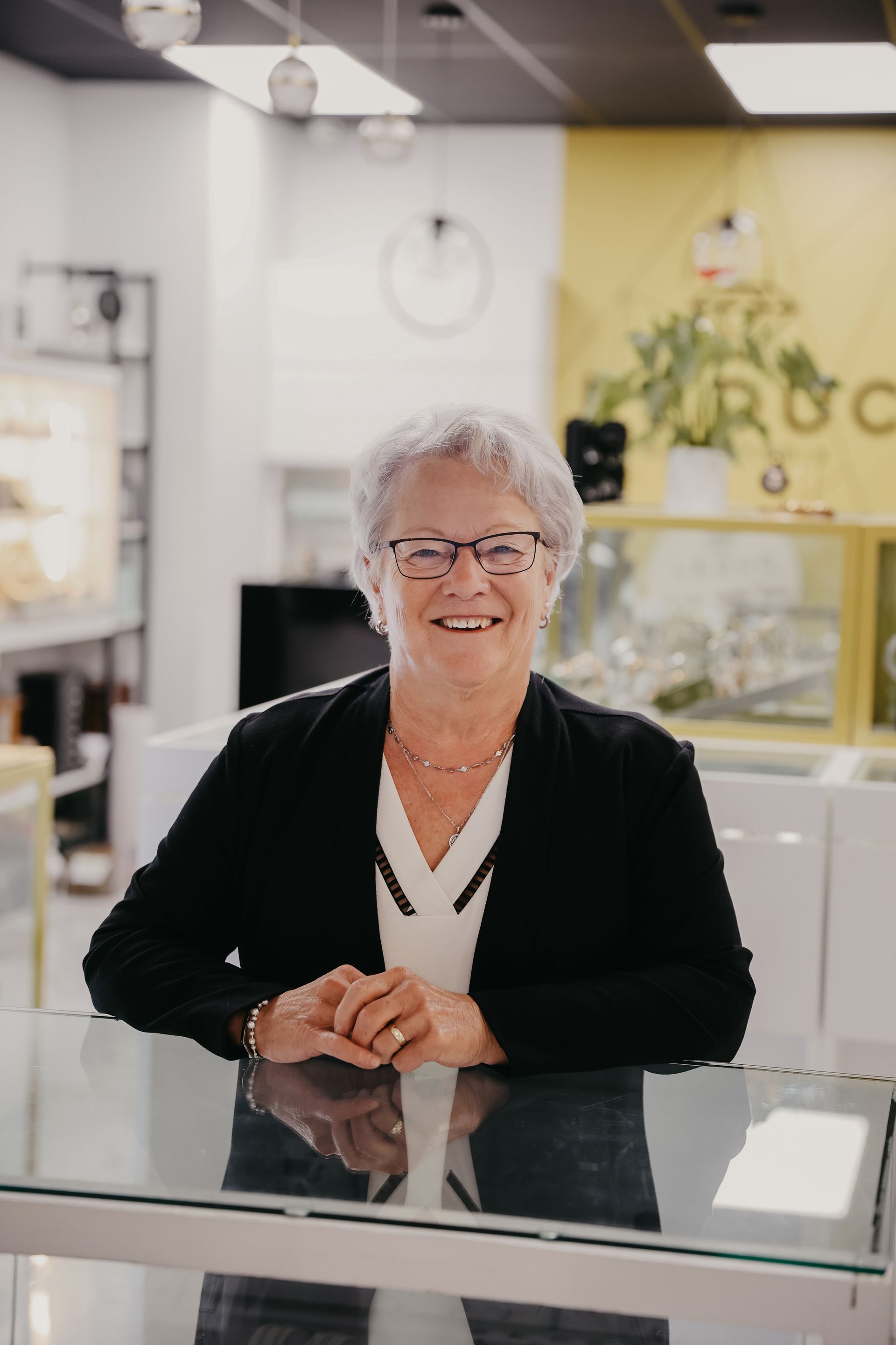 Une femme sourit derrière un comptoir en verre dans un magasin aux accents jaunes.